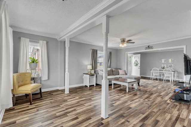 living area featuring baseboards, wood finished floors, crown molding, a textured ceiling, and ornate columns