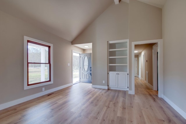 interior space featuring light wood finished floors, baseboards, visible vents, and high vaulted ceiling