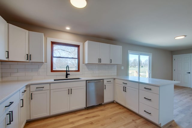 kitchen with light wood finished floors, plenty of natural light, a peninsula, stainless steel dishwasher, and a sink