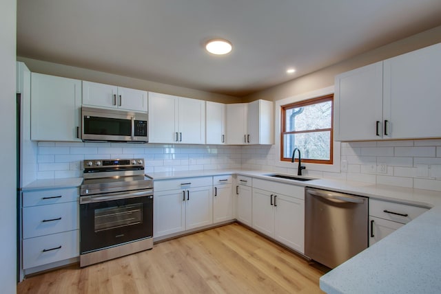 kitchen featuring decorative backsplash, appliances with stainless steel finishes, white cabinetry, a sink, and light wood-type flooring