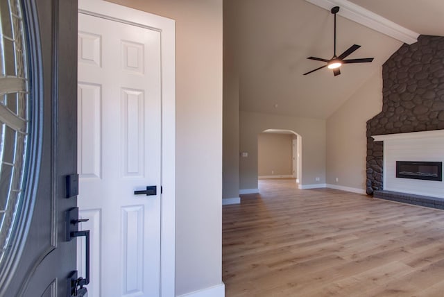 unfurnished living room with arched walkways, vaulted ceiling with beams, a glass covered fireplace, ceiling fan, and wood finished floors