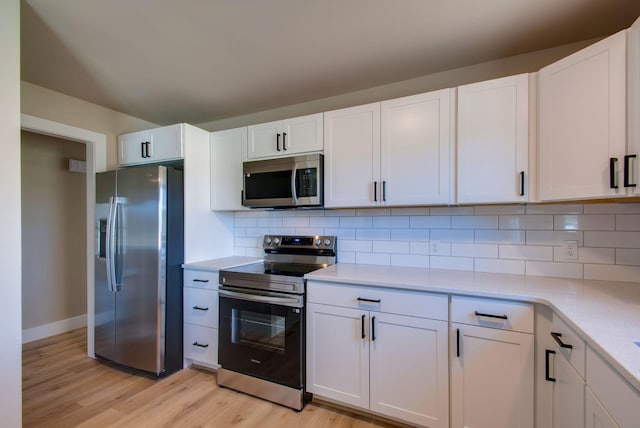 kitchen featuring appliances with stainless steel finishes, white cabinets, light wood-style flooring, and decorative backsplash