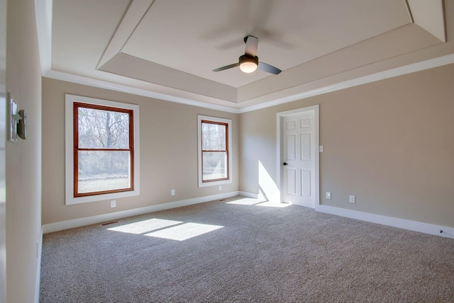 empty room featuring ceiling fan, carpet floors, baseboards, a raised ceiling, and crown molding