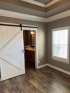 empty room with a barn door, baseboards, crown molding, and wood finished floors