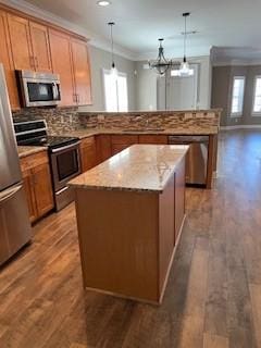 kitchen with a kitchen island, appliances with stainless steel finishes, wood finished floors, a peninsula, and crown molding