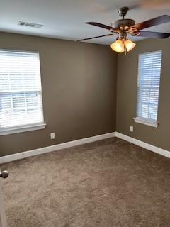 carpeted empty room with a ceiling fan, visible vents, and baseboards