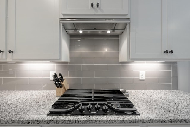 kitchen with white cabinets, stovetop, backsplash, and wall chimney exhaust hood