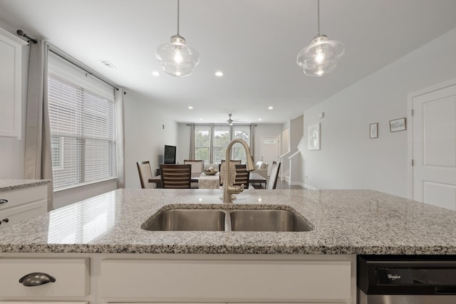 kitchen with pendant lighting, white cabinets, a sink, light stone countertops, and dishwasher