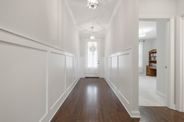 doorway to outside featuring crown molding, wainscoting, dark wood finished floors, and a decorative wall