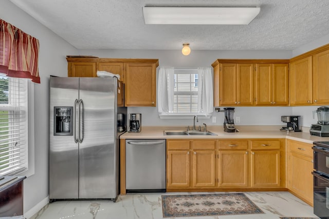 kitchen with a textured ceiling, stainless steel appliances, a sink, marble finish floor, and light countertops