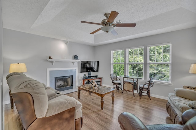 living room with baseboards, a fireplace, a tray ceiling, and wood finished floors