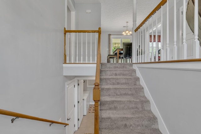 staircase featuring a chandelier, a textured ceiling, and baseboards