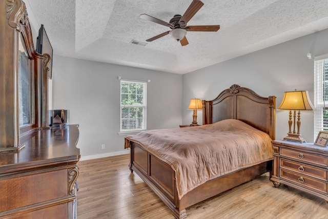 bedroom with visible vents, light wood-style flooring, baseboards, and a textured ceiling