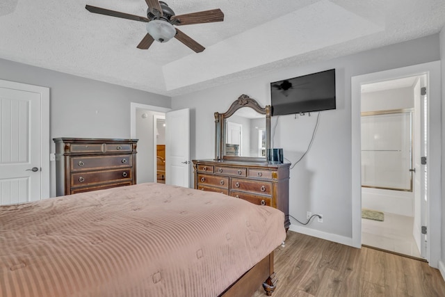 bedroom featuring baseboards, a raised ceiling, ceiling fan, wood finished floors, and a textured ceiling