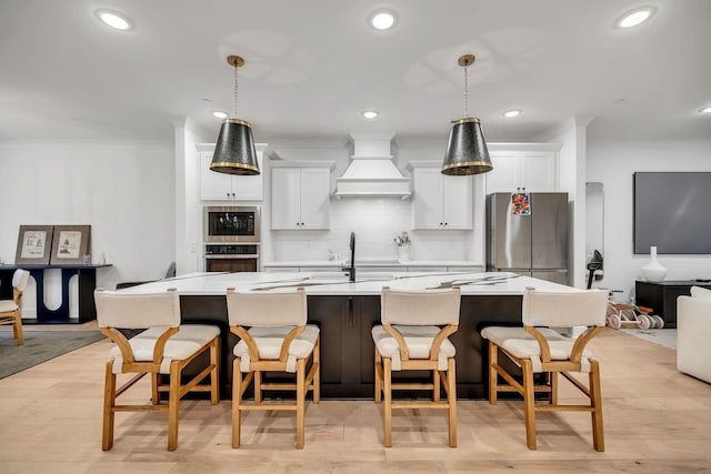 kitchen featuring an island with sink, custom exhaust hood, stainless steel appliances, and ornamental molding