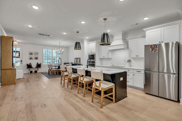 kitchen with custom exhaust hood, stainless steel appliances, light countertops, visible vents, and a kitchen bar