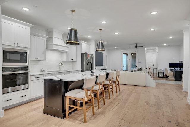 kitchen featuring stainless steel appliances, a kitchen breakfast bar, open floor plan, light wood finished floors, and an island with sink