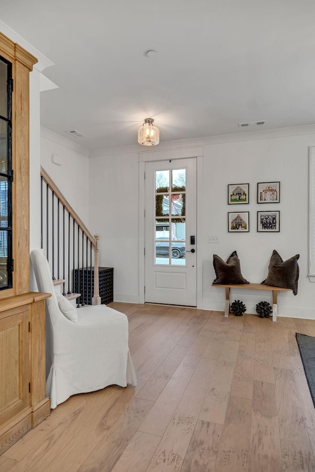 entryway with stairs, crown molding, visible vents, and light wood-style floors