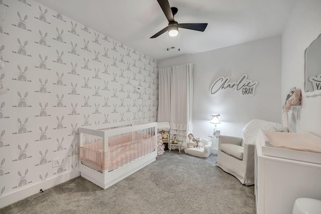 carpeted bedroom with ceiling fan, a crib, baseboards, and wallpapered walls