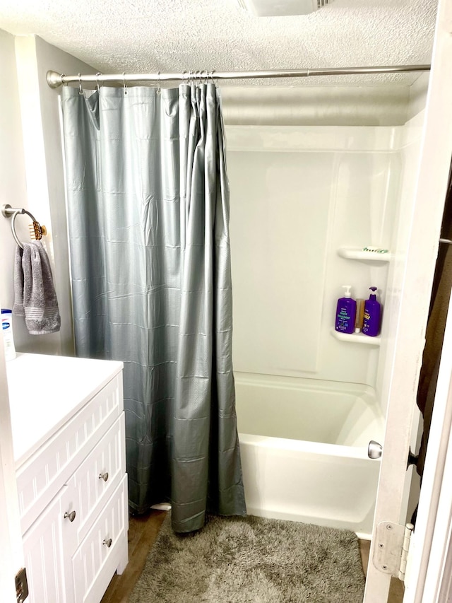 bathroom with shower / bath combination with curtain, a textured ceiling, and vanity