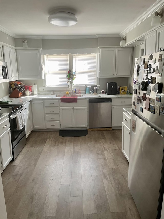 kitchen featuring appliances with stainless steel finishes, light countertops, crown molding, light wood-style floors, and a sink