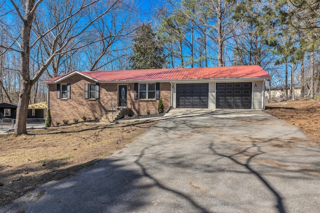 ranch-style home with metal roof, driveway, brick siding, and an attached garage