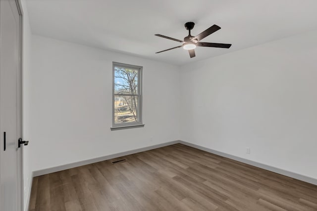 unfurnished room with a ceiling fan, visible vents, baseboards, and wood finished floors