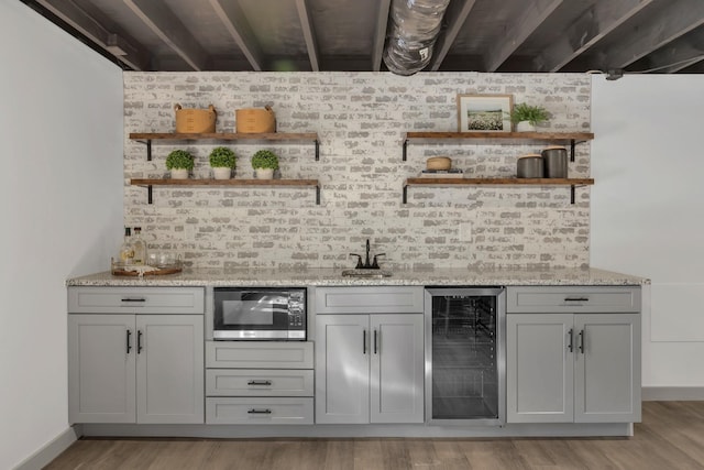 bar featuring beverage cooler, stainless steel microwave, light wood-style flooring, and a bar