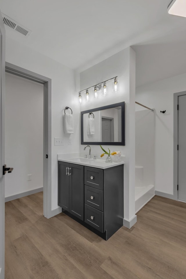 full bath with a shower, visible vents, vanity, wood finished floors, and baseboards