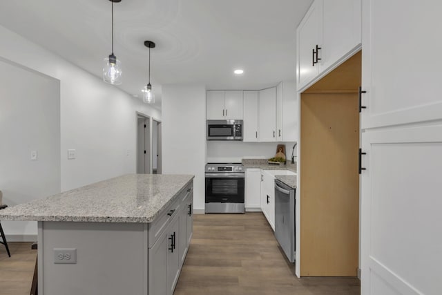 kitchen featuring light stone counters, light wood-style flooring, appliances with stainless steel finishes, a center island, and decorative light fixtures