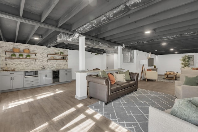 living room featuring beverage cooler, brick wall, light wood-type flooring, and wet bar