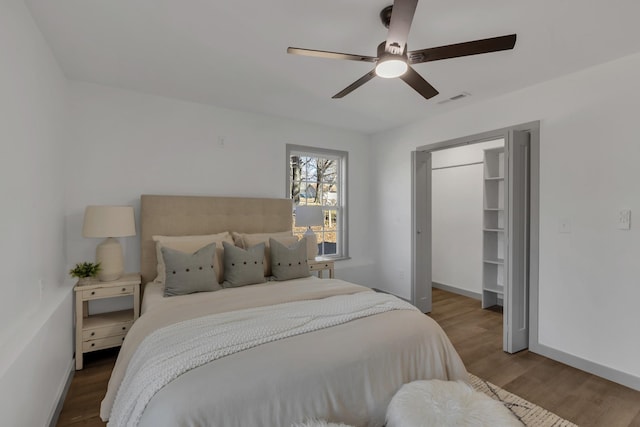 bedroom featuring ceiling fan, wood finished floors, visible vents, baseboards, and a walk in closet