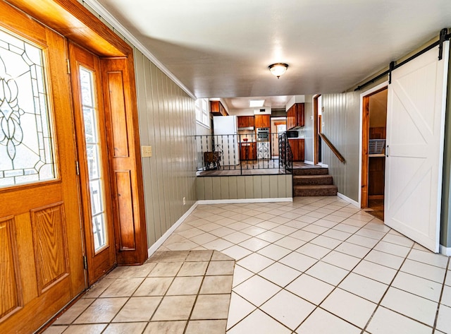 entrance foyer featuring light tile patterned floors, a barn door, stairway, and wood walls