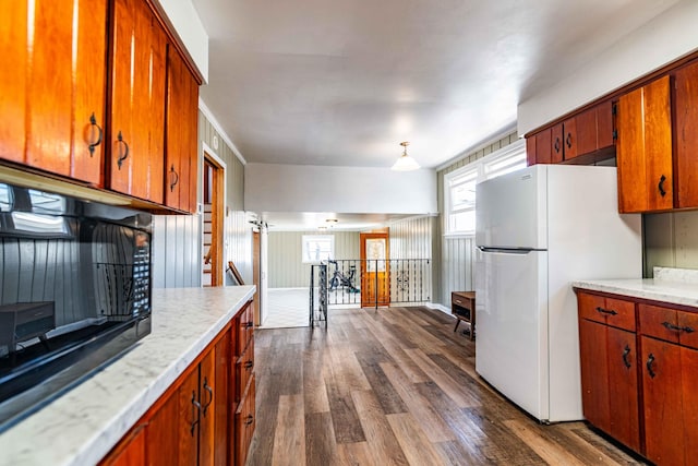 kitchen featuring brown cabinetry, freestanding refrigerator, dark wood-style flooring, and light countertops