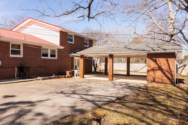 back of house featuring aphalt driveway, an attached carport, brick siding, and fence