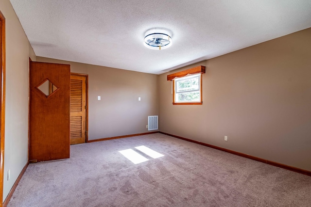 carpeted spare room featuring baseboards, visible vents, and a textured ceiling