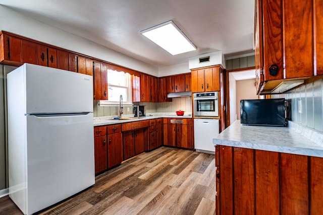 kitchen with white appliances, light countertops, a sink, and wood finished floors