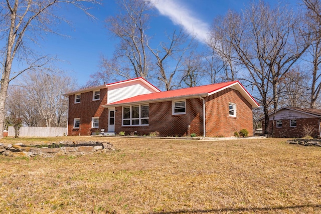 rear view of house featuring brick siding, a yard, and fence