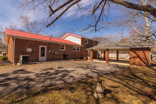 rear view of house with metal roof, aphalt driveway, cooling unit, brick siding, and a carport