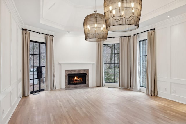 unfurnished living room with visible vents, a raised ceiling, wood finished floors, an inviting chandelier, and a decorative wall