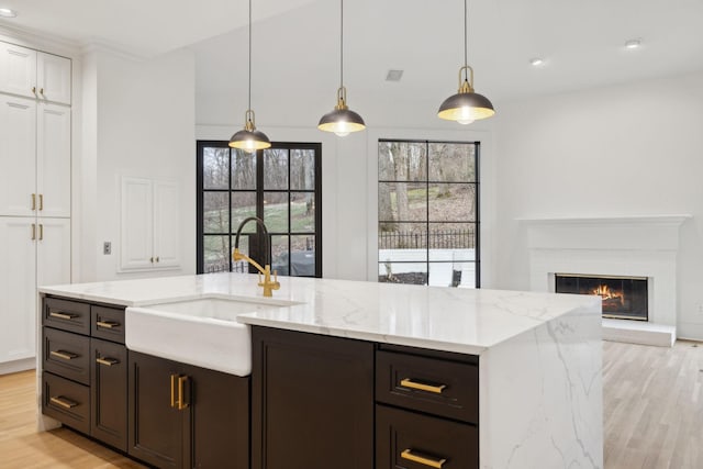 kitchen with a fireplace, a sink, light stone countertops, light wood finished floors, and pendant lighting