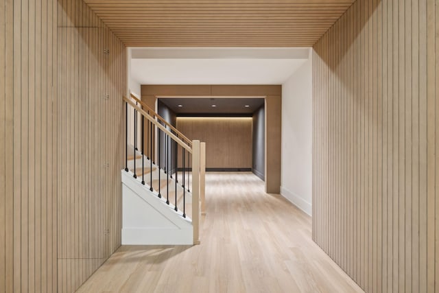 hall with stairs, wooden walls, wood finished floors, and baseboards