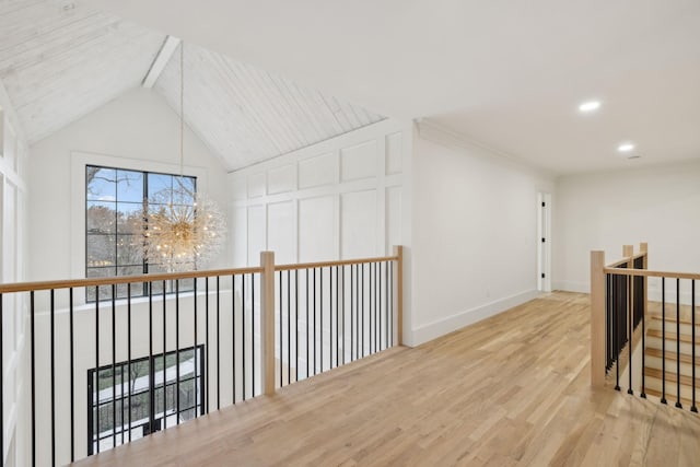 hall featuring baseboards, wood finished floors, an inviting chandelier, vaulted ceiling, and an upstairs landing