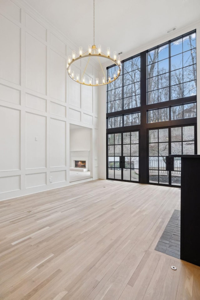 unfurnished living room featuring a warm lit fireplace, light wood-style flooring, a decorative wall, visible vents, and a wall of windows