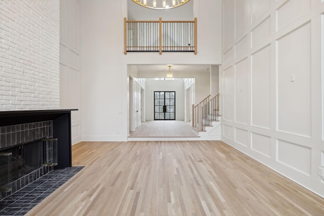 entrance foyer featuring light wood finished floors, a decorative wall, a towering ceiling, a tile fireplace, and stairs