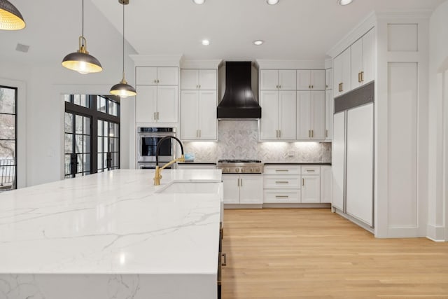 kitchen featuring built in fridge, stainless steel gas cooktop, a sink, white cabinets, and custom exhaust hood