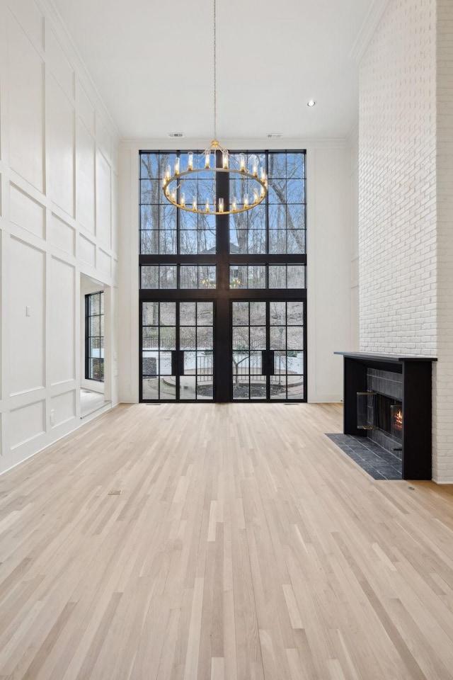 unfurnished living room featuring crown molding, a decorative wall, an inviting chandelier, a fireplace with flush hearth, and wood finished floors