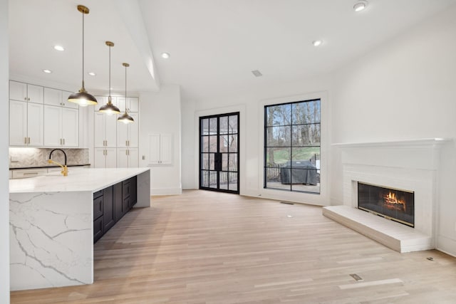 kitchen featuring tasteful backsplash, white cabinets, a spacious island, open floor plan, and light stone countertops