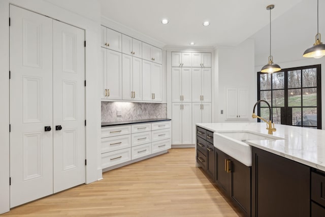 kitchen featuring pendant lighting, light wood finished floors, tasteful backsplash, white cabinetry, and a sink