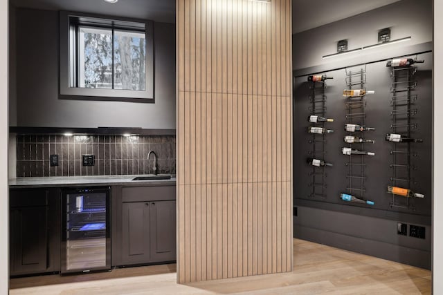 wine area featuring light wood-style floors, wine cooler, indoor wet bar, and a sink